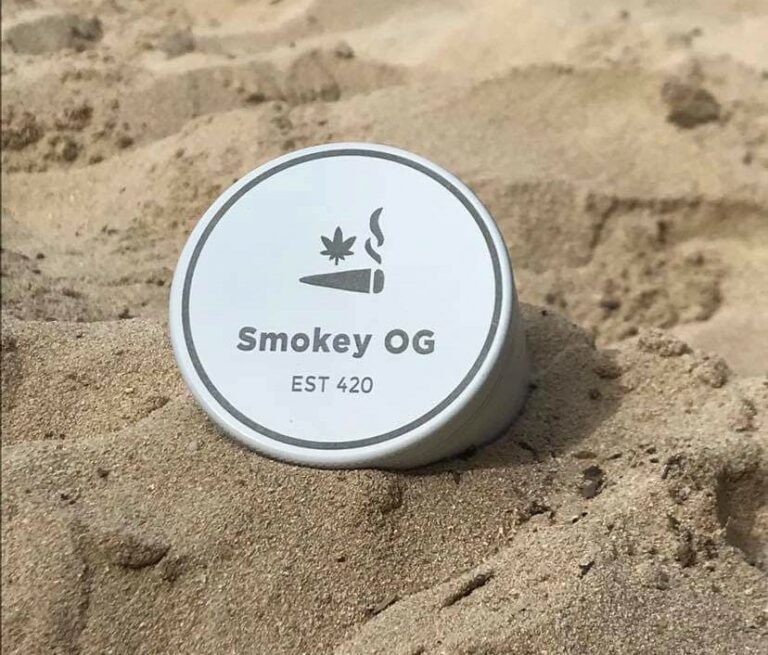 White balm tin in the sand with words Smokey OG